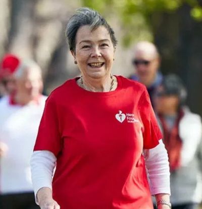 Smiling woman in a red Heart Foundation shirt leading a walking group in a park