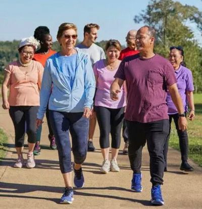 Group of about eight people of different ages and cultures walking together in a park, smiling and talking